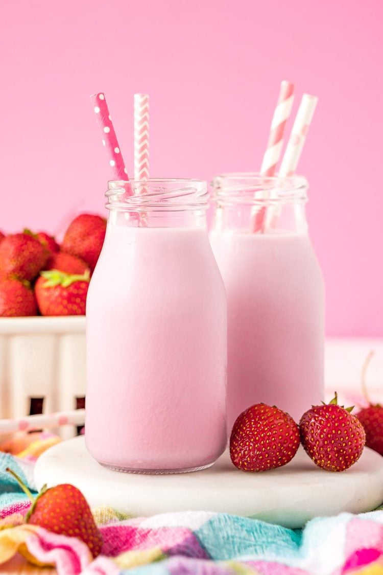 Close up photo of two milk bottles of homemade strawberry milk on a white board.