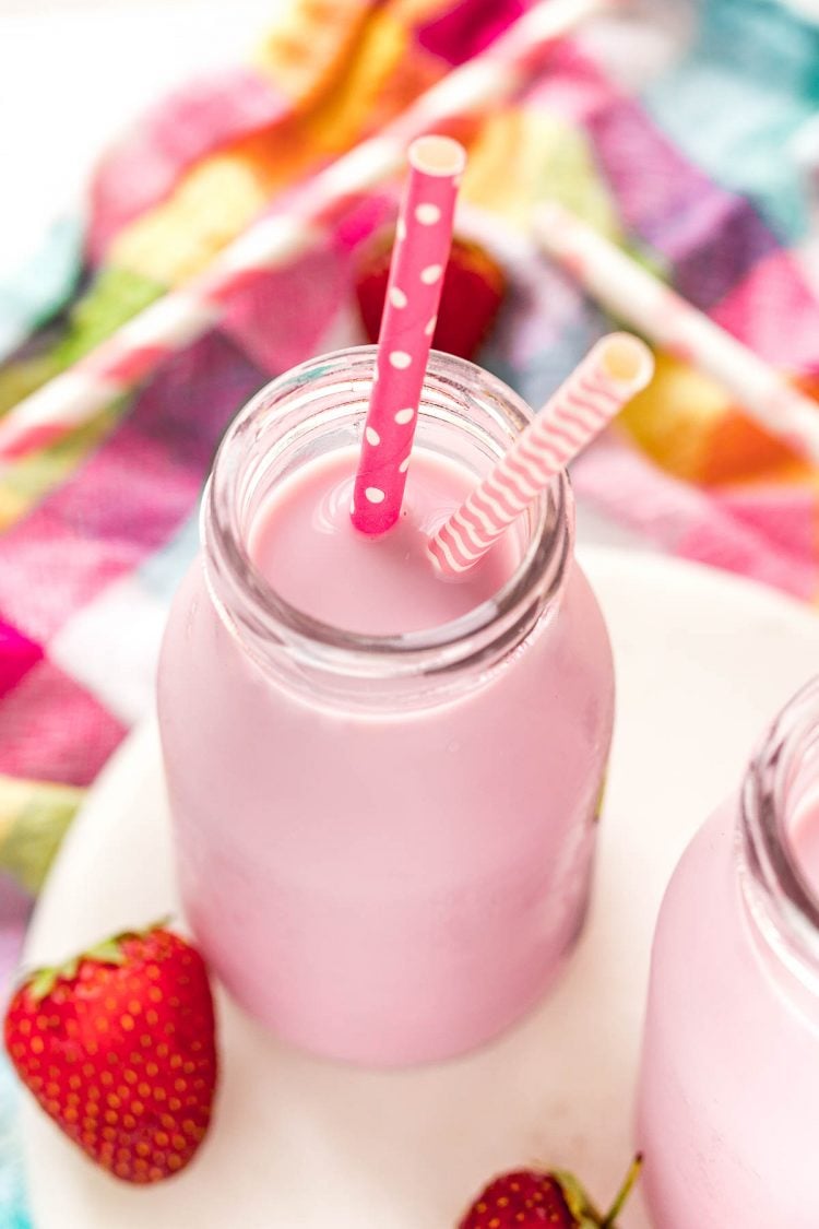 Close up photo of a milk bottle with strawberry milk in it on a white marble board on a colored checkered napkin.