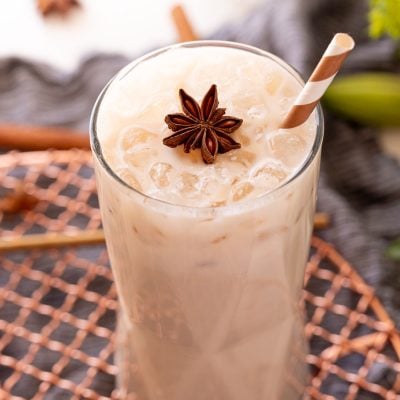 Close up photo of a glass with an iced chai latte in it topped with a star anise and a straw.