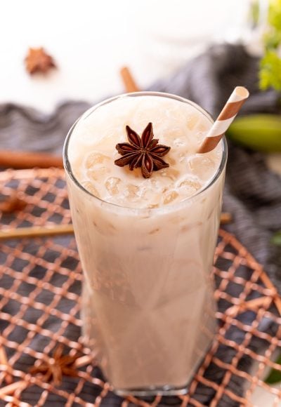 Close up photo of a glass with an iced chai latte in it topped with a star anise and a straw.