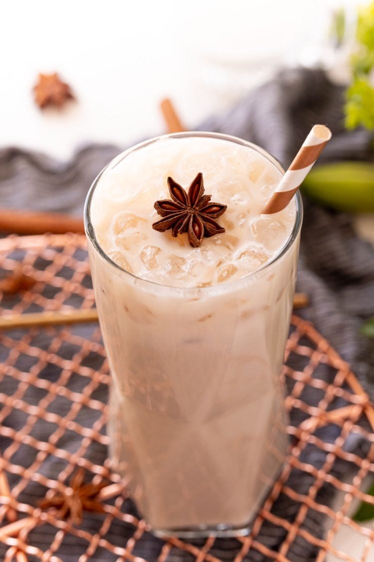 Close up photo of a glass with an iced chai latte in it topped with a star anise and a straw.