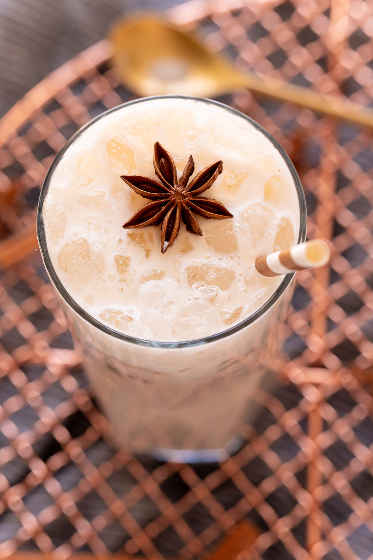 Close up photo of an iced chai tea latte on a copper wire rack garnished with star anise and a straw.