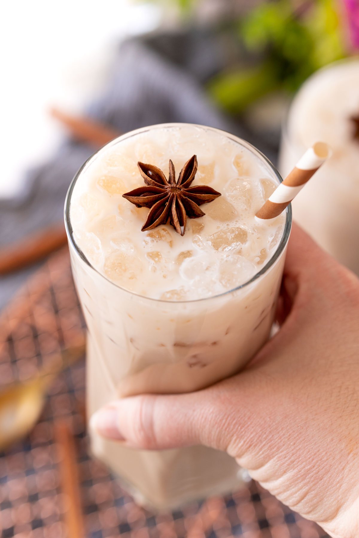 A woman's hand holding a glass with an iced chai latte to the camera.