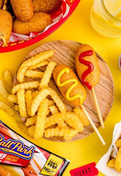 Close up photo of mini corn dogs on a wooden plate with crinkle fries.