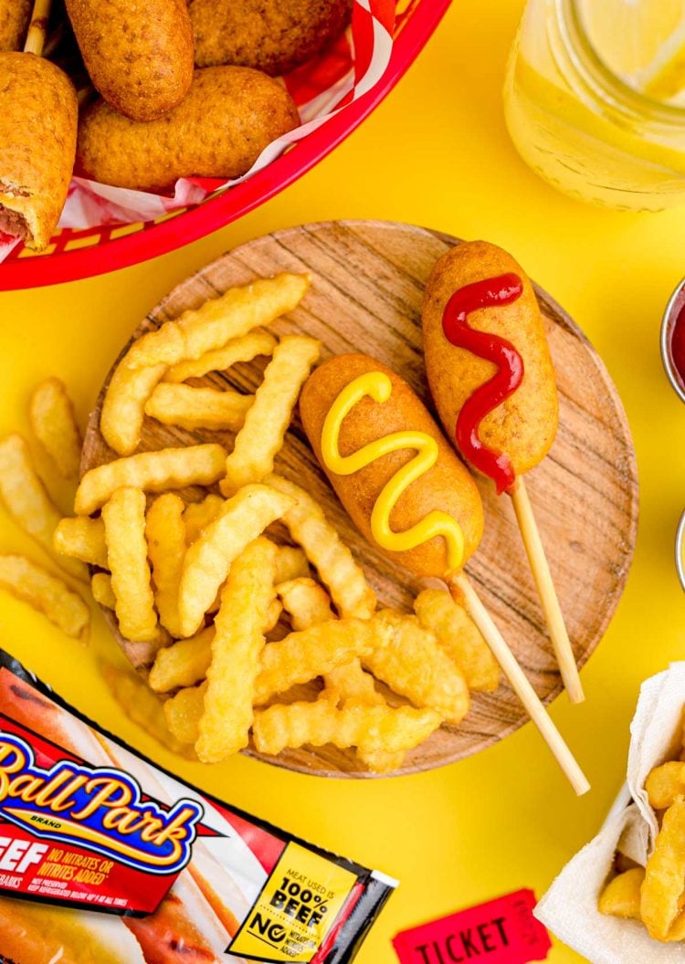Close up photo of mini corn dogs on a wooden plate with crinkle fries.