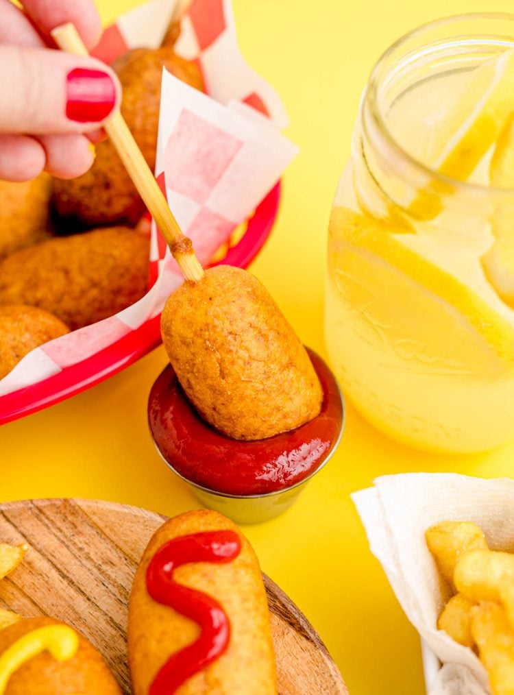 A mini corndog being dipped in a small bowl of ketchup.