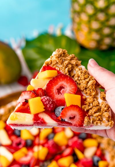 Close up photo of a woman's hand holding a piece of nature's pizza to the camera.