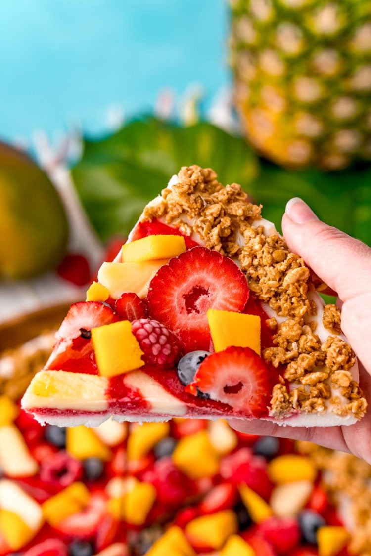 Close up photo of a woman's hand holding a piece of nature's pizza to the camera.