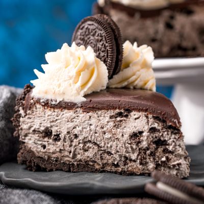 Close up photo of a slice of no bake oreo cheesecake on a gray plate on a gray napkin with oreos around it.