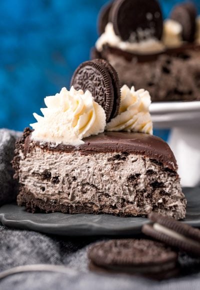 Close up photo of a slice of no bake oreo cheesecake on a gray plate on a gray napkin with oreos around it.