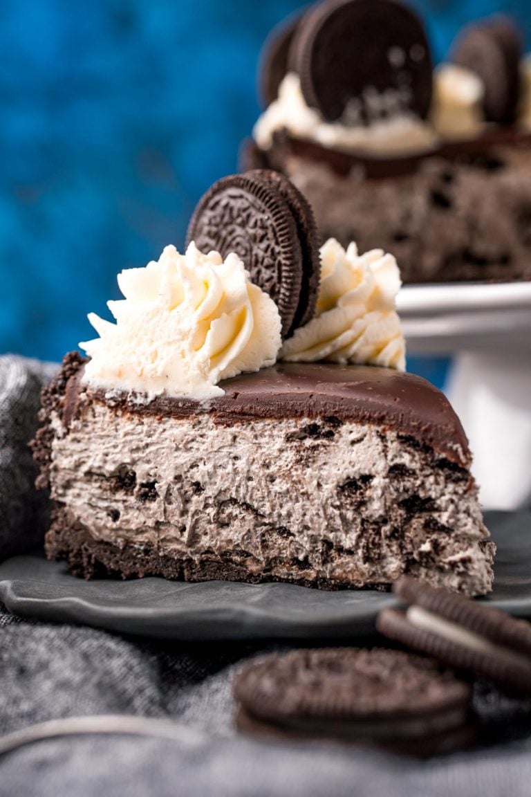 Close up photo of a slice of no bake oreo cheesecake on a gray plate on a gray napkin with oreos around it.