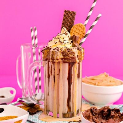 Photo of a peanut butter freakshake on a pink surface surrounded by sweet toppings.