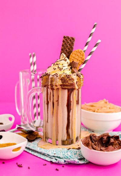 Photo of a peanut butter freakshake on a pink surface surrounded by sweet toppings.