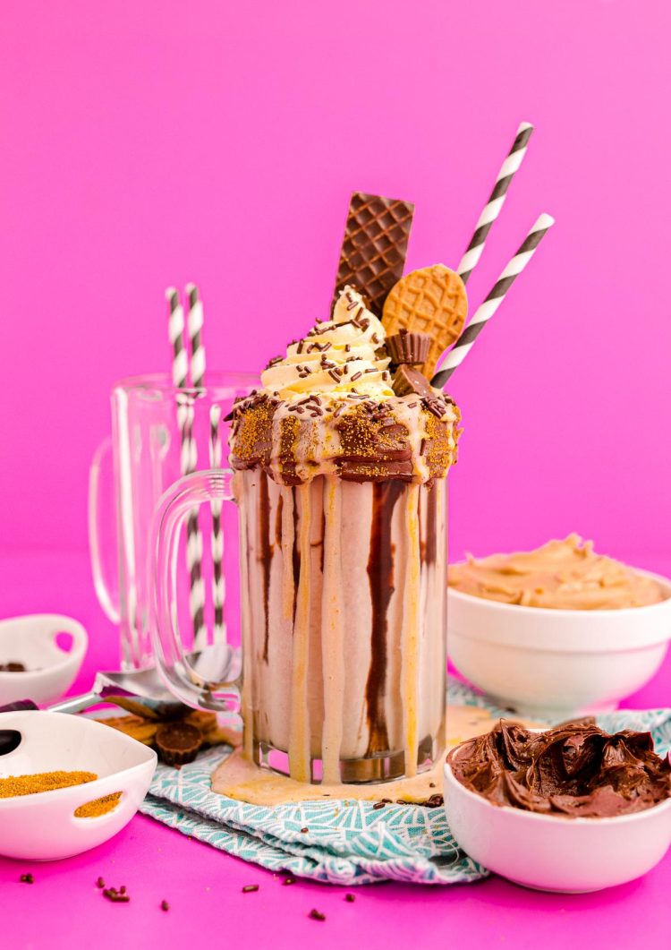 Photo of a peanut butter freakshake on a pink surface surrounded by sweet toppings.