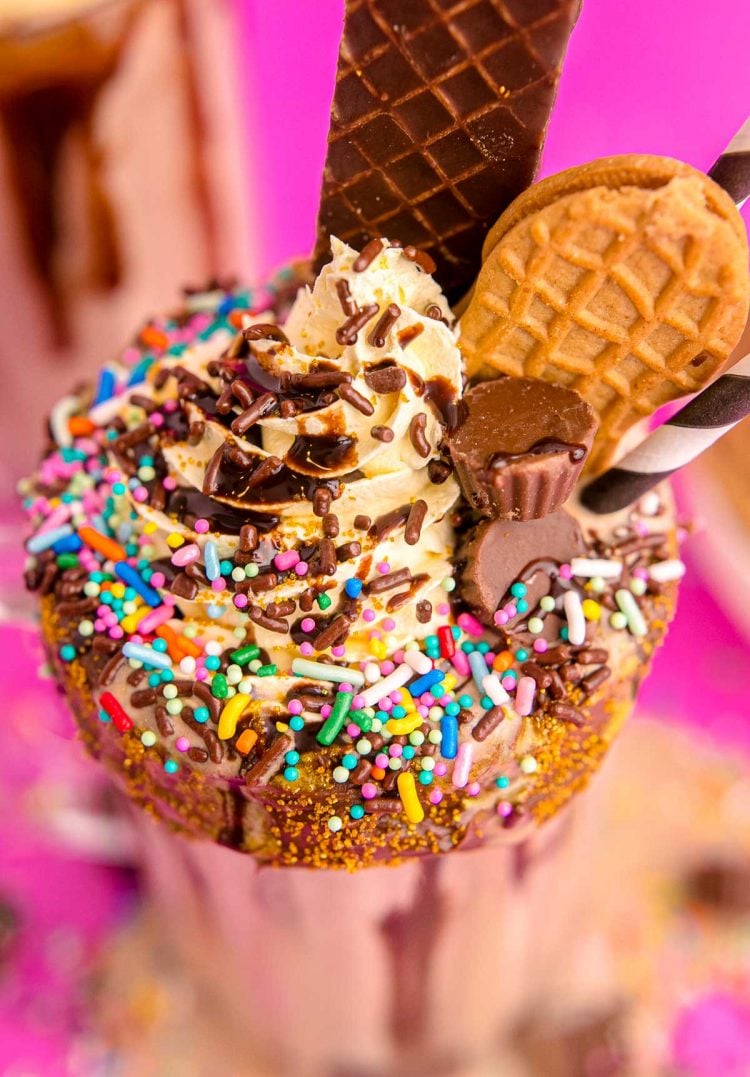 Close up photo of a peanut butter milkshake topped with whipped cream, sprinkles, chocolate candy and cookies, and chocolate sauce.