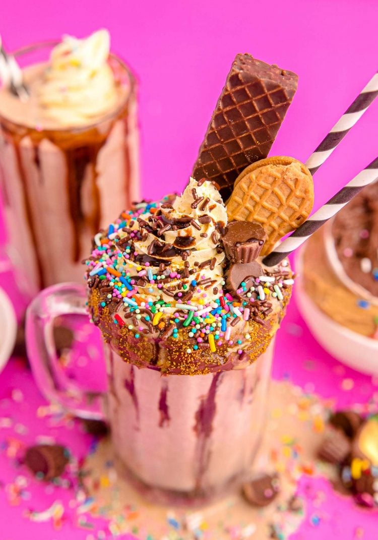 Close up photo of a peanut butter milkshake topped with candy, cookies, whipped cream, and sprinkles.