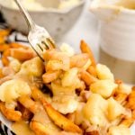 Close up photo of poutine with a fork taking a bite out of it.
