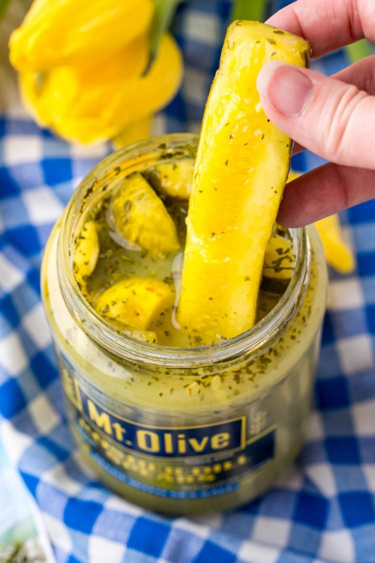 A woman's hand pulling a ranch pickles out of a jar.