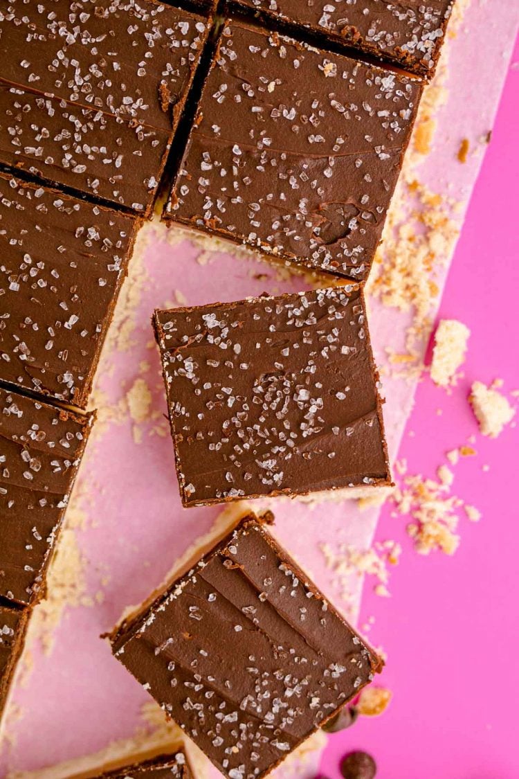 Overhead photo of millionaire shortbread bars on a piece of parchment paper on a pink surface.