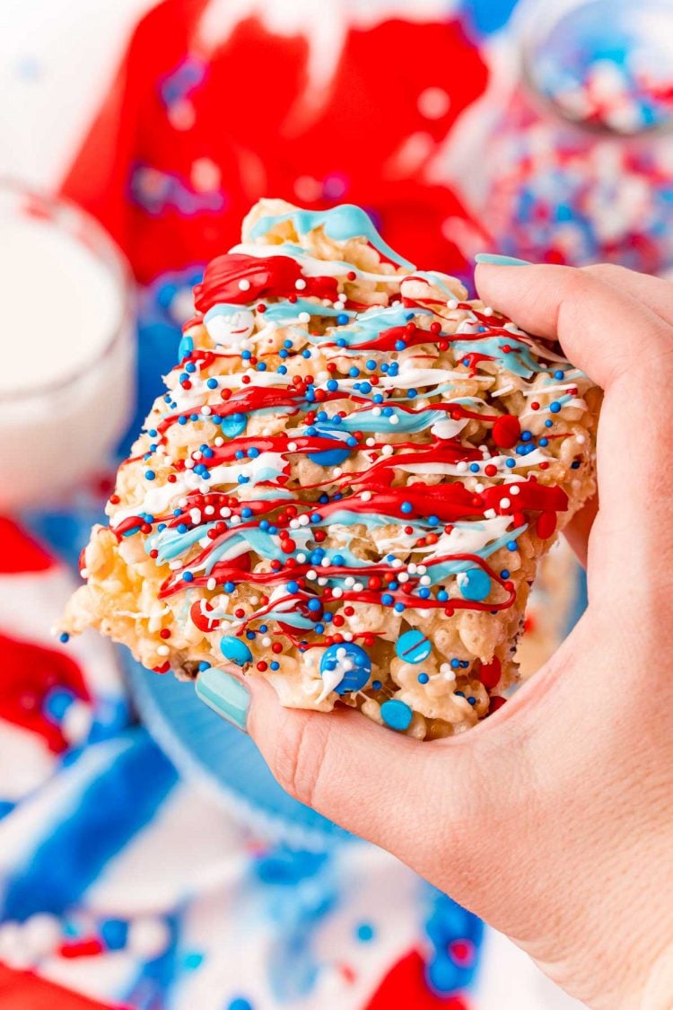 A woman's hand holding a red, white, and blue rice krispie treat to the camera.