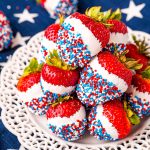 Close up photo of a while plate on a blue and what star napkin with strawberries that have been dipped in white candy then in red, white, and blue sprinkles.
