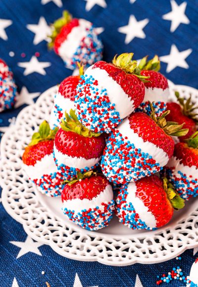 Close up photo of a while plate on a blue and what star napkin with strawberries that have been dipped in white candy then in red, white, and blue sprinkles.