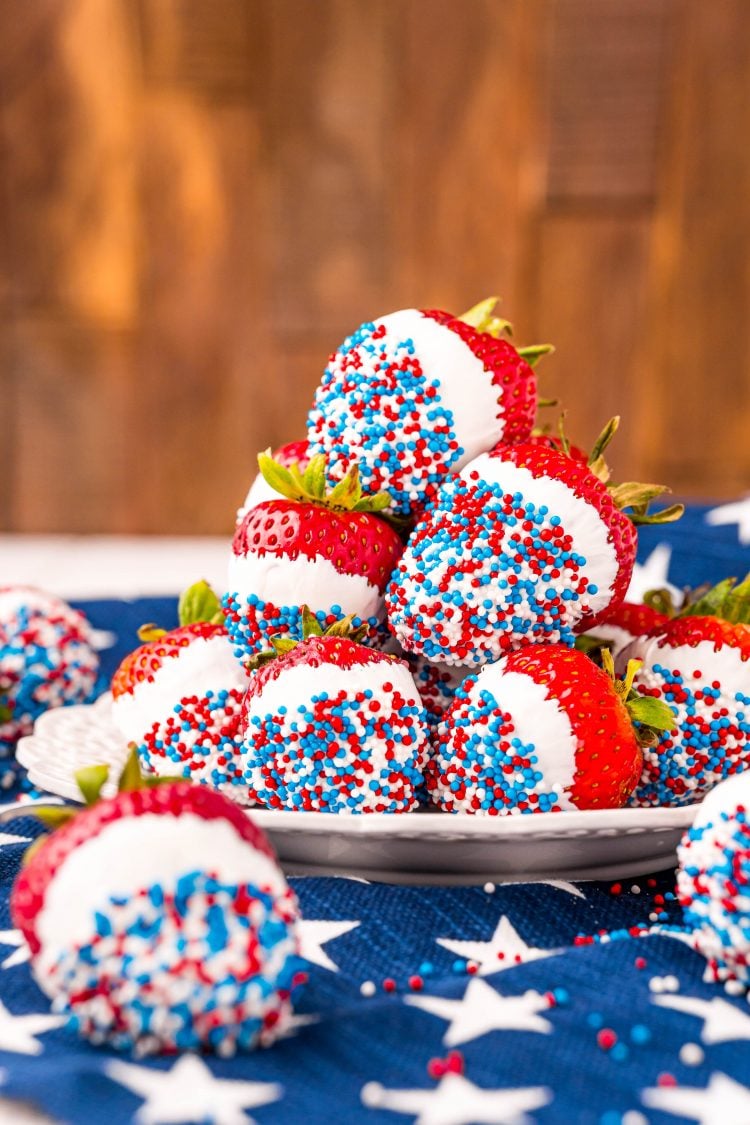 Strawberries dipped in white chocolate and red, white, and blue sprinkles on a white plate on a blue and white star napkin.