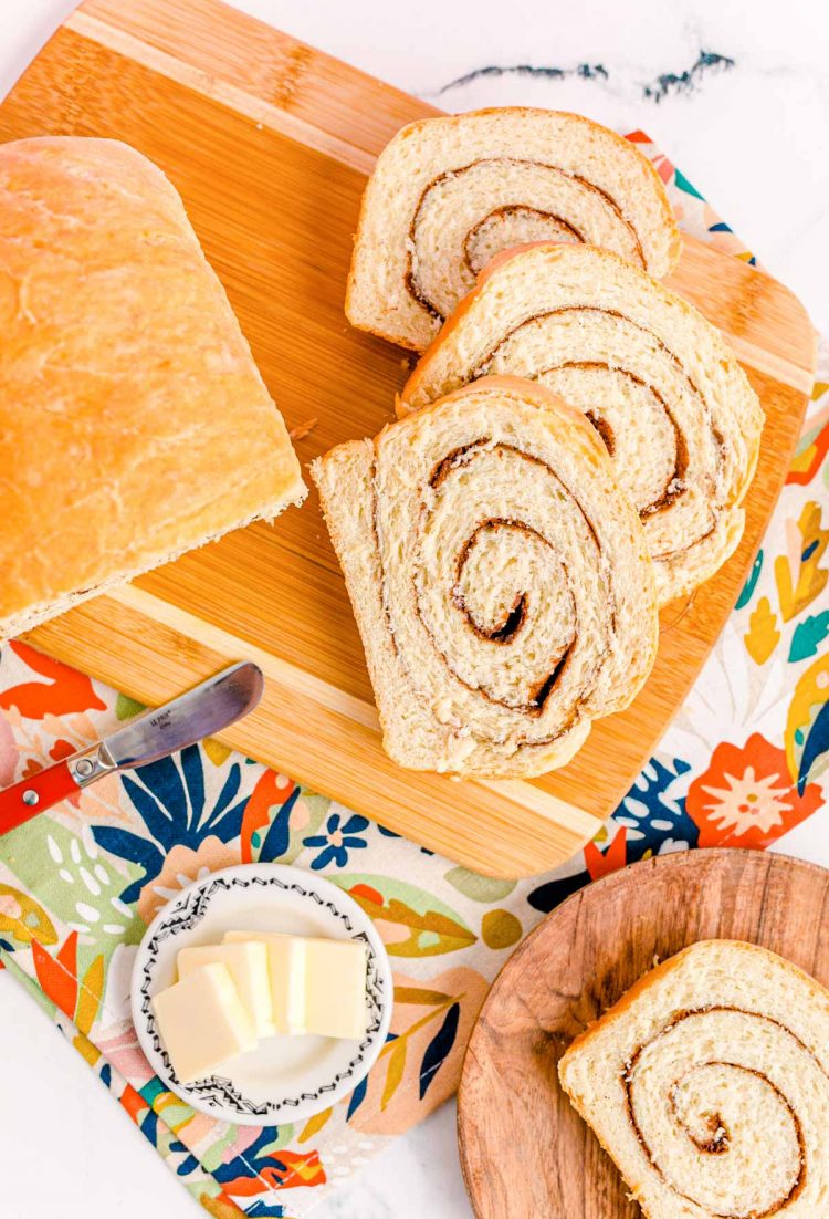 Overhead photo of a partial loaf and slices of cinnamon swirl bread on a cutting board on a floral napkin.