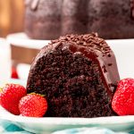 Close up photo of a slice of chocolate cake on a white plate with strawberries.