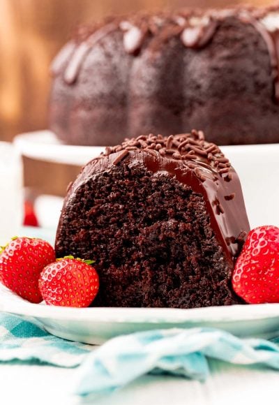 Close up photo of a slice of chocolate cake on a white plate with strawberries.