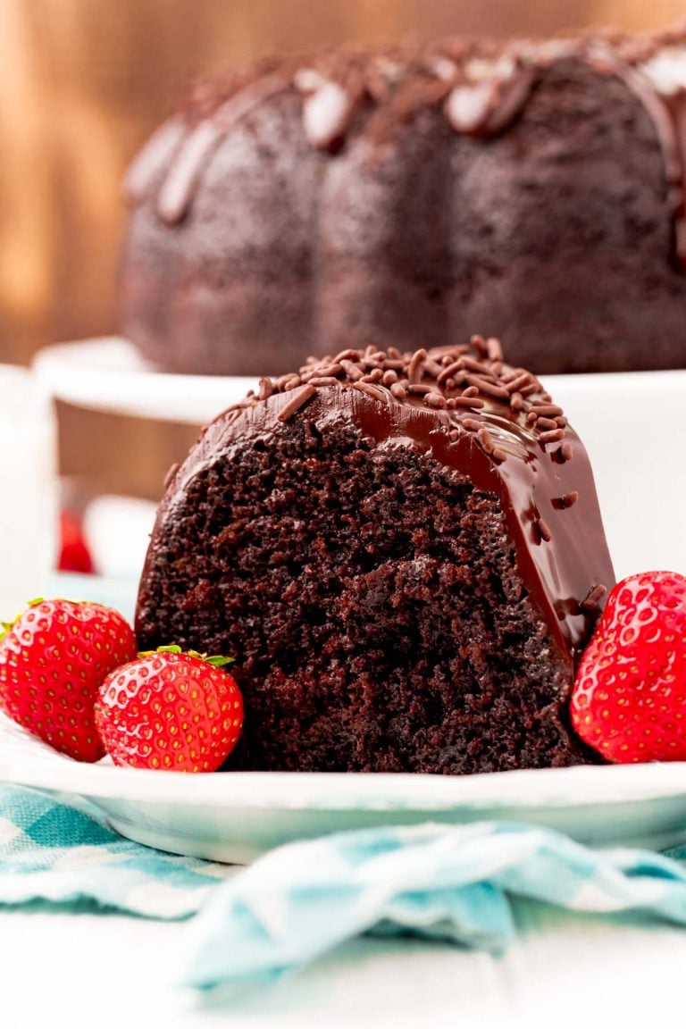 Close up photo of a slice of chocolate cake on a white plate with strawberries.
