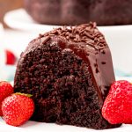 Close up photo of a slice of chocolate cake on a white plate with strawberries.