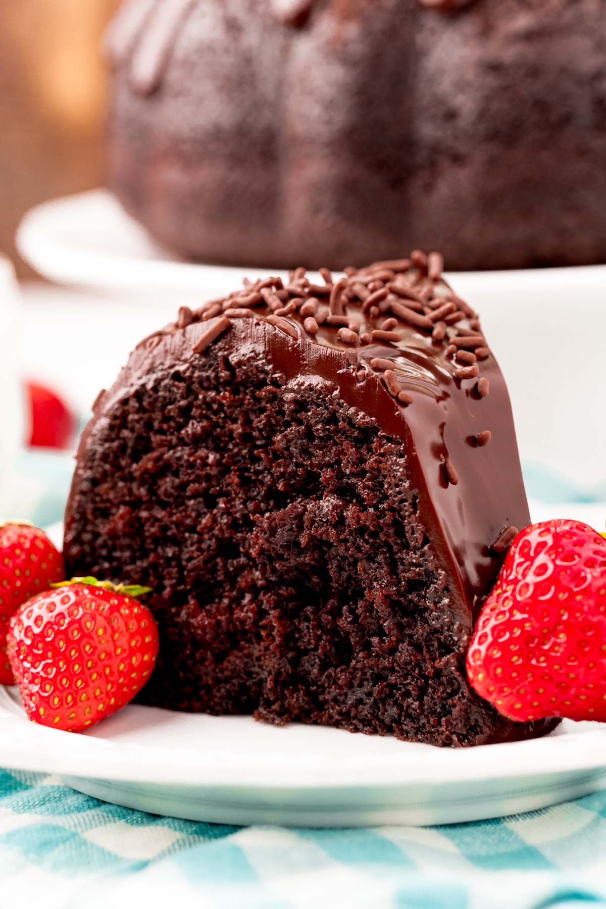 Close up photo of a slice of chocolate cake on a white plate with strawberries.