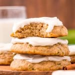 Close up photo of a stack of three zucchini cookies with frosting on a wooden plate on a blue napkin.