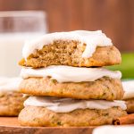 Close up photo of a stack of three zucchini cookies with frosting on a wooden plate on a blue napkin.