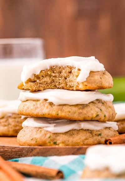 Close up photo of a stack of three zucchini cookies with frosting on a wooden plate on a blue napkin.