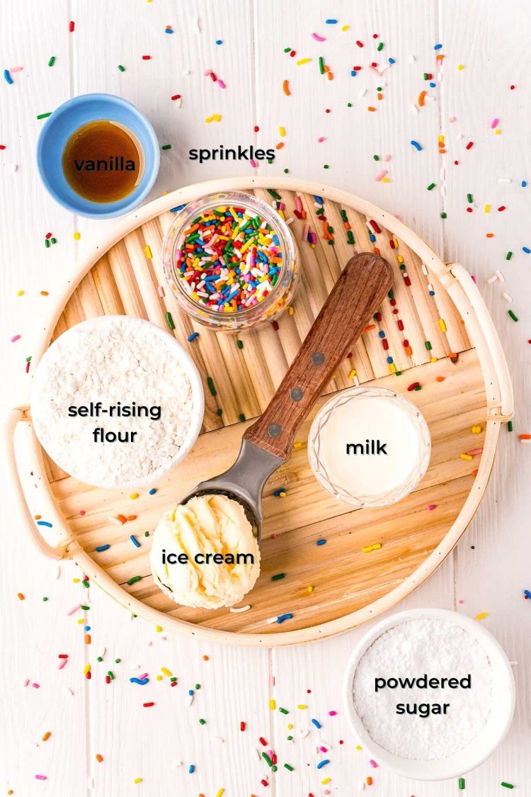 Overhead photo of ingredients used to make funfetti ice cream bread on a white table on a rattan tray with sprinkles scattered all around it.