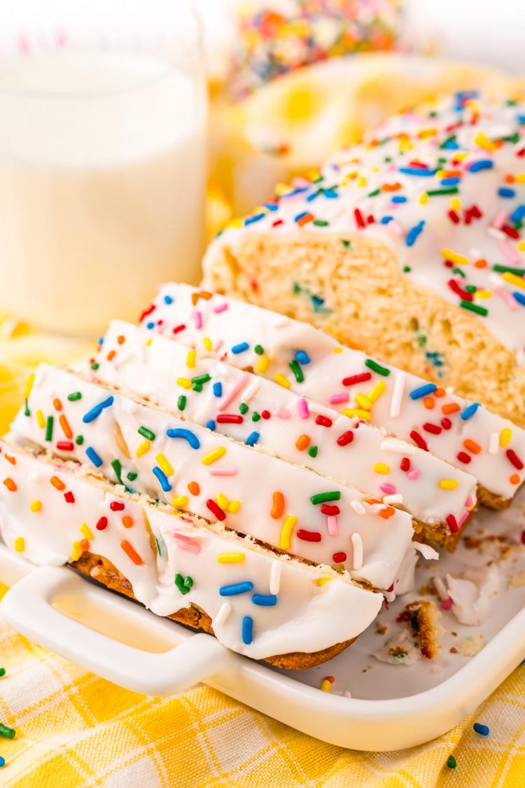 Close up photo of a white plate with a sliced funfetti bread on it with a glass of milk in the background.