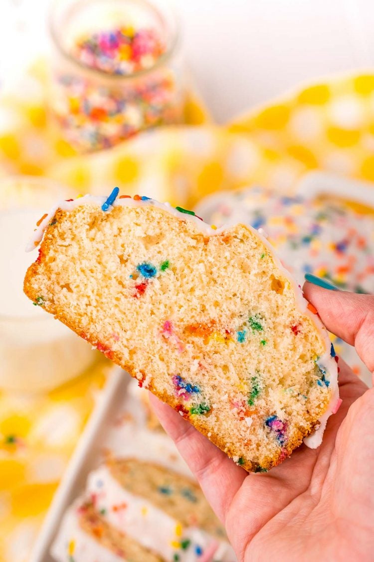 A woman's hand holding a piece of funfetti ice cream bread to the camera.