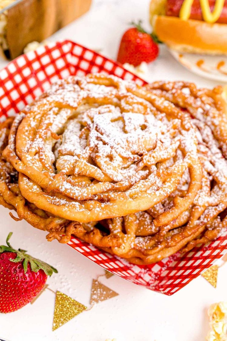 Funnel cakes in a red and white food basket topped with powdered sugar.