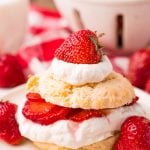 Close up photo of strawberry shortcake on a beige plate on a red and white checkered napkin.
