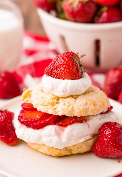 Close up photo of strawberry shortcake on a beige plate on a red and white checkered napkin.