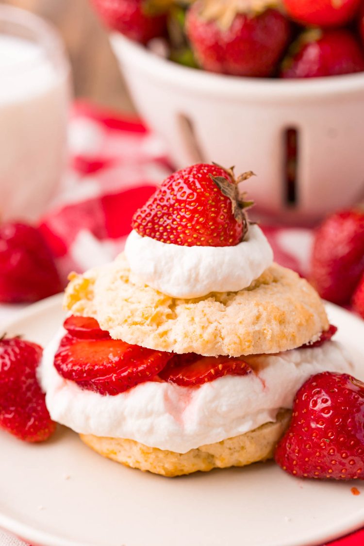 Close up photo of strawberry shortcake on a beige plate on a red and white checkered napkin.