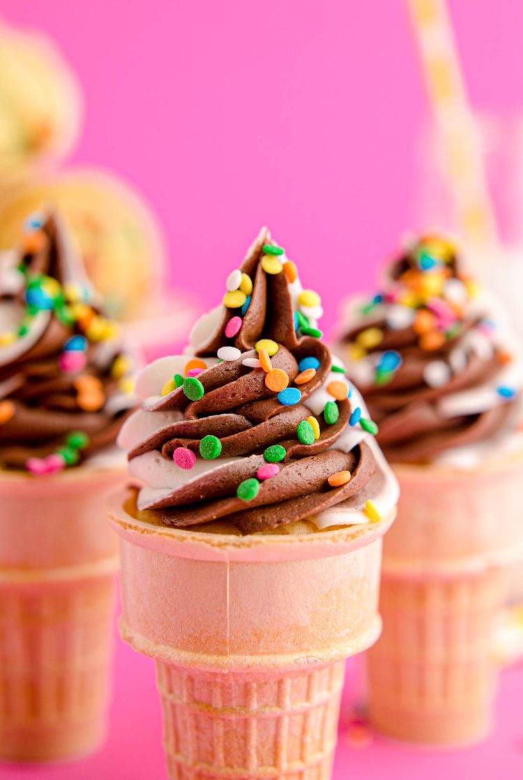 Close up photo of cupcakes in ice cream cones topped with a vanilla and chocolate frosting.