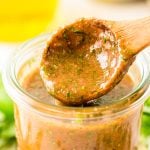 Close up photo of a jar with Italian marinade for chicken in it with a wooden spoon scooping out a little.
