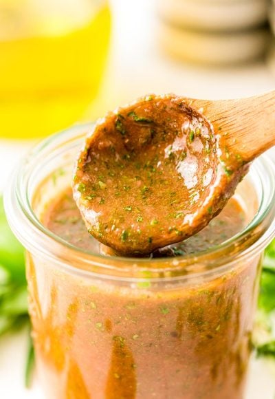 Close up photo of a jar with Italian marinade for chicken in it with a wooden spoon scooping out a little.