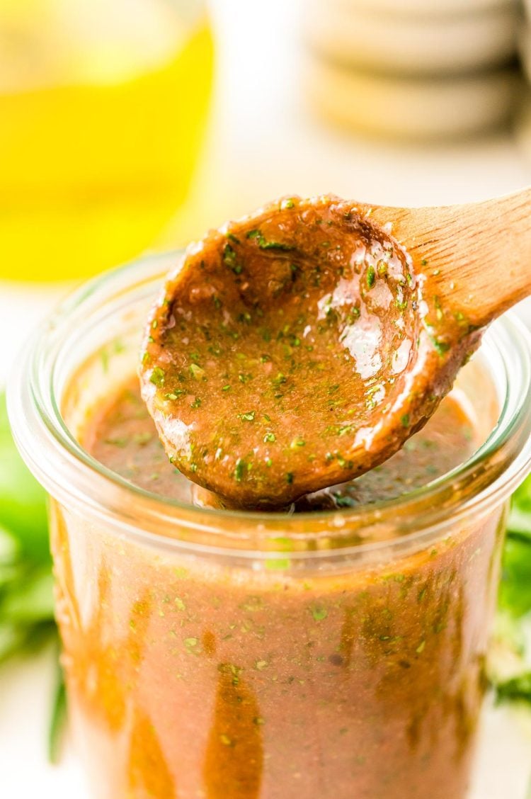 Close up photo of a jar with Italian marinade for chicken in it with a wooden spoon scooping out a little.