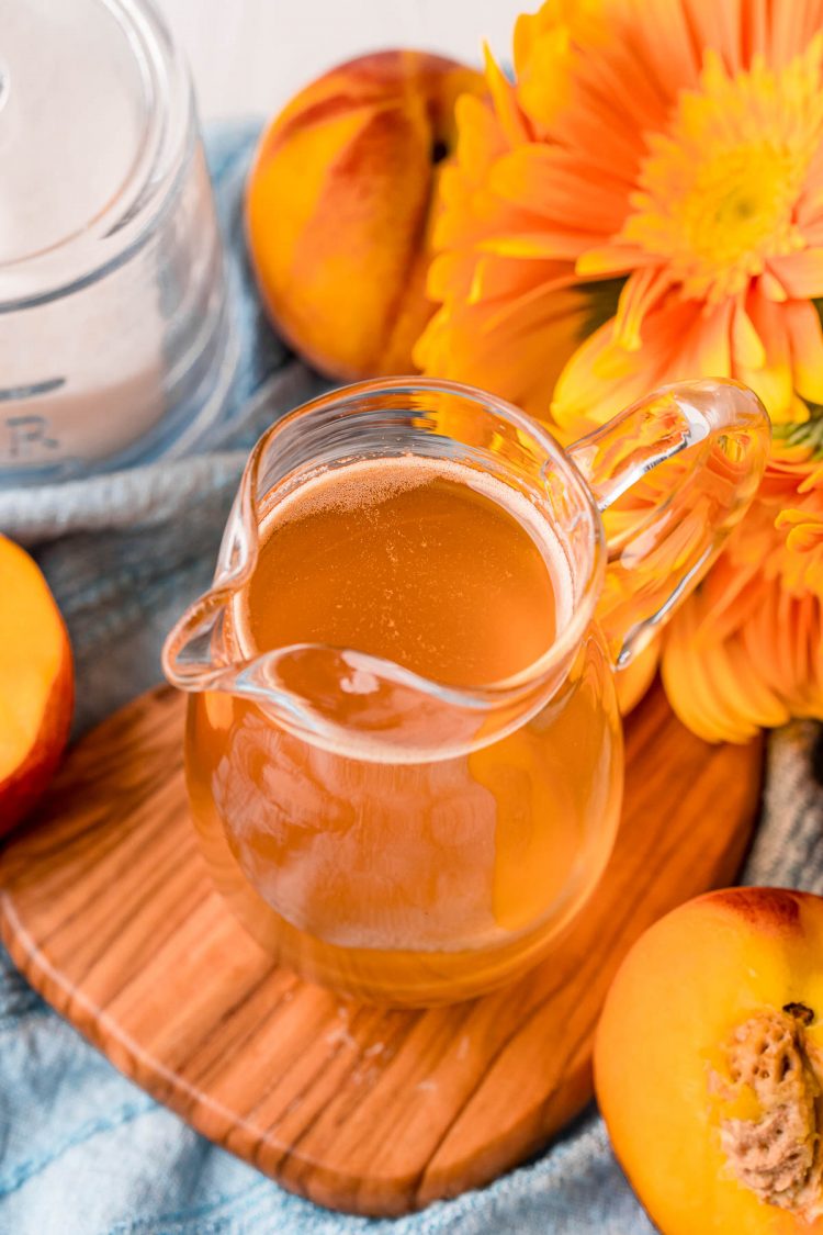 Small pitcher of peach simple syrup on a wooden board on a blue napkin.