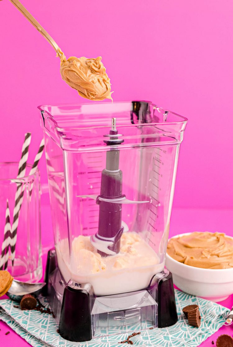 A scoop of peanut butter being added to a blender with milk and ice cream to make a peanut butter milkshake.