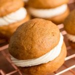 Close up photo of a pumpkin whoopie pie on a copper wire rack with more in the background.